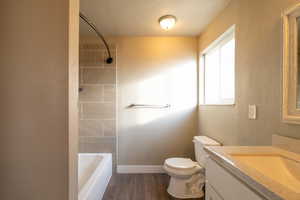 Full bathroom featuring tiled shower / bath combo, hardwood / wood-style floors, a textured ceiling, toilet, and vanity