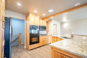 Kitchen featuring light brown cabinets, sink, decorative backsplash, light wood-type flooring, and appliances with stainless steel finishes