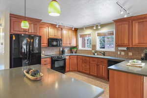 Kitchen with decorative backsplash, a textured ceiling, black appliances, hanging light fixtures, and light tile patterned flooring