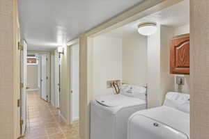 Laundry room featuring light tile patterned flooring, washing machine and dryer, and a textured ceiling