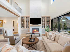 Living room with plenty of natural light, a stone fireplace, light wood-type flooring, and a high ceiling