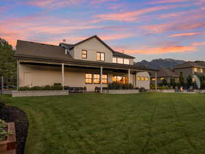 Back house at dusk with a lawn and a patio area