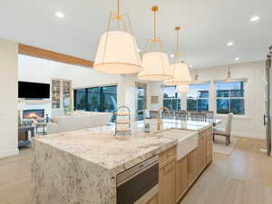 Kitchen featuring sink, light stone counters, light hardwood / wood-style flooring, pendant lighting, and a kitchen island with sink