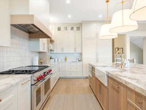 Kitchen featuring white cabinets, wall chimney range hood, hanging light fixtures, light hardwood / wood-style floors, and stainless steel appliances