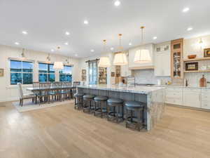 Kitchen with pendant lighting, a large island with sink, white cabinets, light hardwood / wood-style flooring, and light stone counters