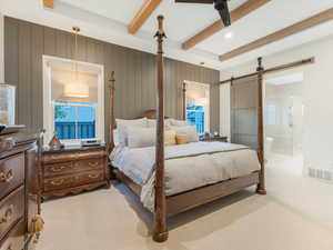 Carpeted bedroom with beamed ceiling, ensuite bathroom, ceiling fan, and a barn door