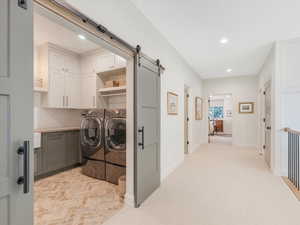 Washroom with washer and clothes dryer, a barn door, cabinets, and light carpet