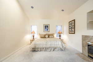 Carpeted bedroom with multiple windows, a high end fireplace, and vaulted ceiling