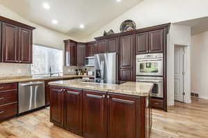 Kitchen with a center island, sink, light hardwood / wood-style flooring, vaulted ceiling, and stainless steel appliances