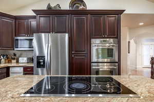 Kitchen with lofted ceiling, backsplash, french doors, light stone countertops, and appliances with stainless steel finishes