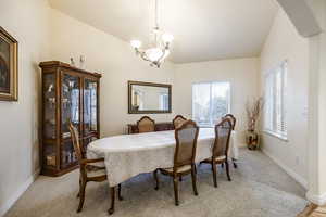 Carpeted dining room featuring a chandelier and vaulted ceiling