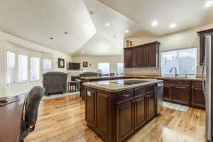 Kitchen with light wood-type flooring, black electric cooktop, sink, a center island, and lofted ceiling