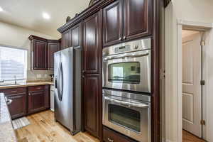 Kitchen featuring light stone countertops, tasteful backsplash, stainless steel appliances, sink, and light hardwood / wood-style floors