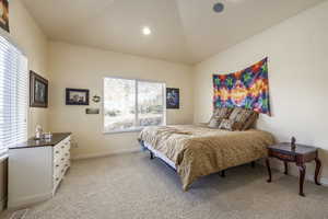 Carpeted bedroom featuring vaulted ceiling and multiple windows