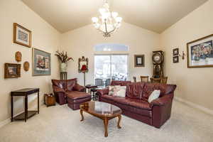 Carpeted living room featuring vaulted ceiling and a notable chandelier