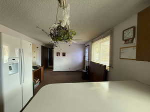 Kitchen with white fridge with ice dispenser, a textured ceiling, and dark colored carpet