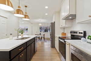 Kitchen featuring appliances with stainless steel finishes, custom exhaust hood, sink, pendant lighting, and white cabinets