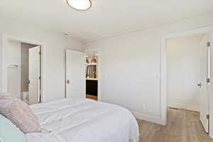 Bedroom with light hardwood / wood-style floors, stainless steel refrigerator, and ensuite bath