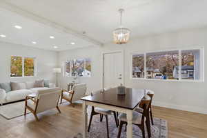 Dining area with beamed ceiling, light wood-type flooring, an inviting chandelier, and a healthy amount of sunlight