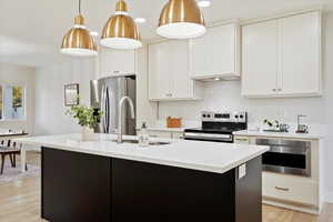 Kitchen featuring pendant lighting, white cabinets, light wood-type flooring, an island with sink, and stainless steel appliances