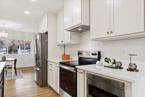 Kitchen featuring light stone countertops, stainless steel appliances, light hardwood / wood-style flooring, premium range hood, and white cabinets