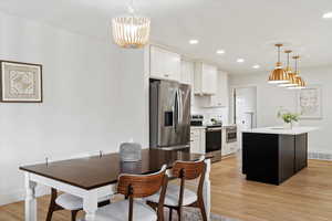 Kitchen featuring white cabinets, decorative light fixtures, stainless steel appliances, and an island with sink