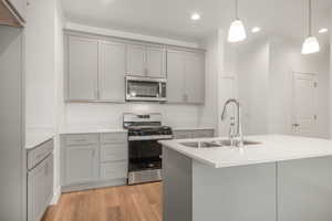 Kitchen featuring gray cabinetry, sink, light wood-type flooring, decorative light fixtures, and stainless steel appliances