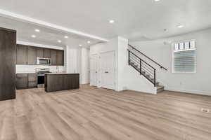 Kitchen with appliances with stainless steel finishes, dark brown cabinets, sink, a center island with sink, and light hardwood / wood-style flooring