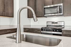 Kitchen with sink, dark brown cabinetry, light stone countertops, and stainless steel appliances