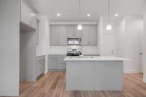 Kitchen featuring white range with gas cooktop, a kitchen island with sink, sink, pendant lighting, and light hardwood / wood-style flooring