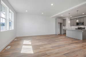 Kitchen featuring gray cabinetry, an island with sink, pendant lighting, appliances with stainless steel finishes, and light wood-type flooring