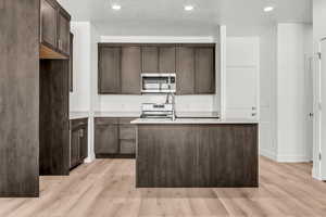 Kitchen featuring a center island with sink, light hardwood / wood-style floors, dark brown cabinetry, and a textured ceiling