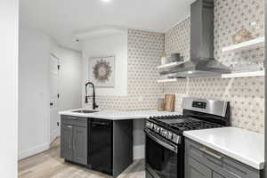 Kitchen featuring light wood-type flooring, wall chimney exhaust hood, sink, black dishwasher, and stainless steel range with gas stovetop