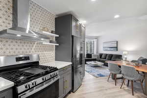 Kitchen featuring appliances with stainless steel finishes, light wood-type flooring, backsplash, wall chimney exhaust hood, and gray cabinetry