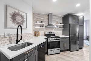 Kitchen featuring backsplash, wall chimney range hood, sink, light hardwood / wood-style flooring, and stainless steel appliances