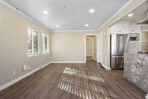 Interior space featuring white cabinets, wall chimney range hood, crown molding, dark hardwood / wood-style flooring, and stainless steel appliances