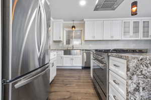 Kitchen with white cabinets, stainless steel appliances, hanging light fixtures, and dark wood-type flooring