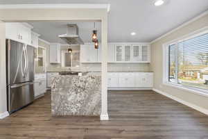 Kitchen with white cabinets, stainless steel refrigerator, and wall chimney exhaust hood