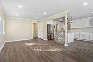 Kitchen featuring stainless steel fridge, dark hardwood / wood-style flooring, crown molding, decorative light fixtures, and white cabinetry