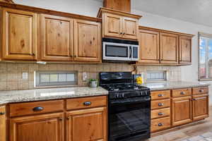 Kitchen featuring black gas range, light stone countertops, light wood-type flooring, and backsplash