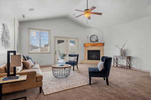 Carpeted living room featuring a tiled fireplace, ceiling fan, french doors, and lofted ceiling