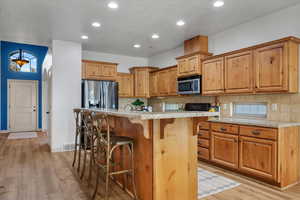 Kitchen with a breakfast bar, a center island, decorative backsplash, light hardwood / wood-style floors, and stainless steel appliances