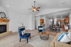 Living room with light carpet, a fireplace, ceiling fan, and vaulted ceiling