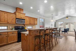 Kitchen with black gas stove, pendant lighting, lofted ceiling, light hardwood / wood-style floors, and a kitchen island