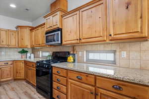 Kitchen with gas stove, tasteful backsplash, light hardwood / wood-style flooring, and light stone counters