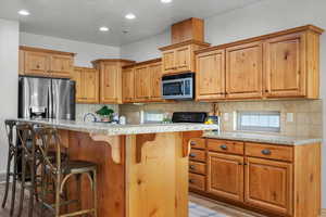 Kitchen featuring light stone countertops, a kitchen breakfast bar, stainless steel appliances, light hardwood / wood-style flooring, and a center island