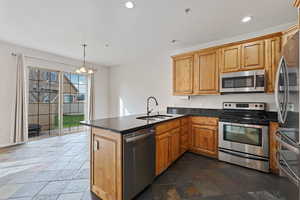 Kitchen with kitchen peninsula, stainless steel appliances, sink, an inviting chandelier, and hanging light fixtures