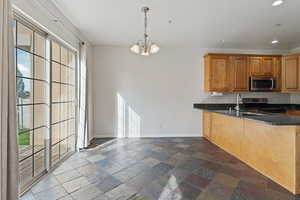 Kitchen with a wealth of natural light, kitchen peninsula, appliances with stainless steel finishes, and a chandelier