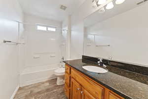 Full bathroom featuring hardwood / wood-style floors, tiled shower / bath combo, toilet, and vanity