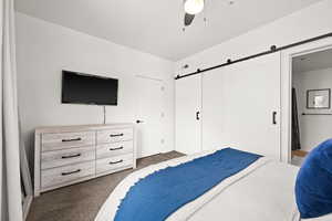 Bedroom featuring dark colored carpet, ceiling fan, and a barn door